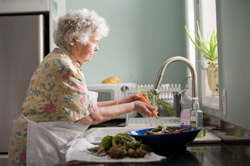 photo of an elderly woman washing fresh vegetables