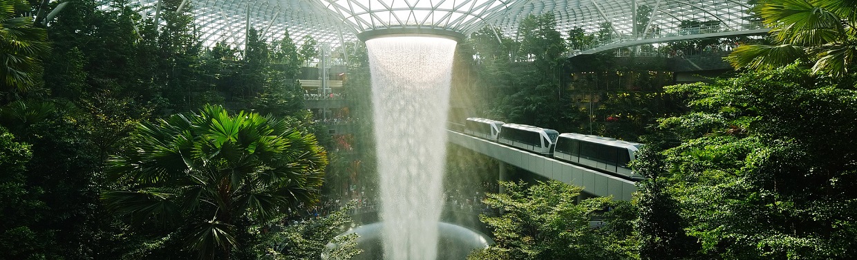 train travelling through giant greenhouse filled with trees, a waterfall at the center